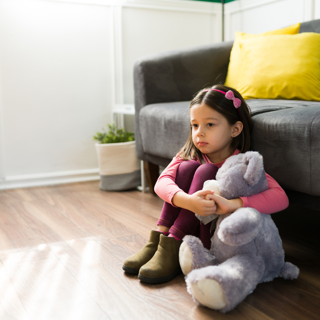 Ein kleines Mädchen mit Teddy, allein am Boden hockend